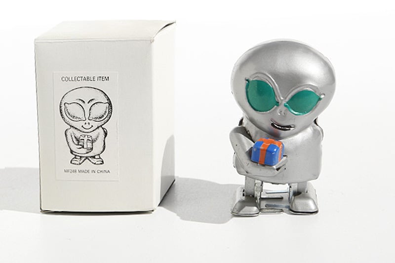 Metallic alien tin toy holding a small gift box with packaging