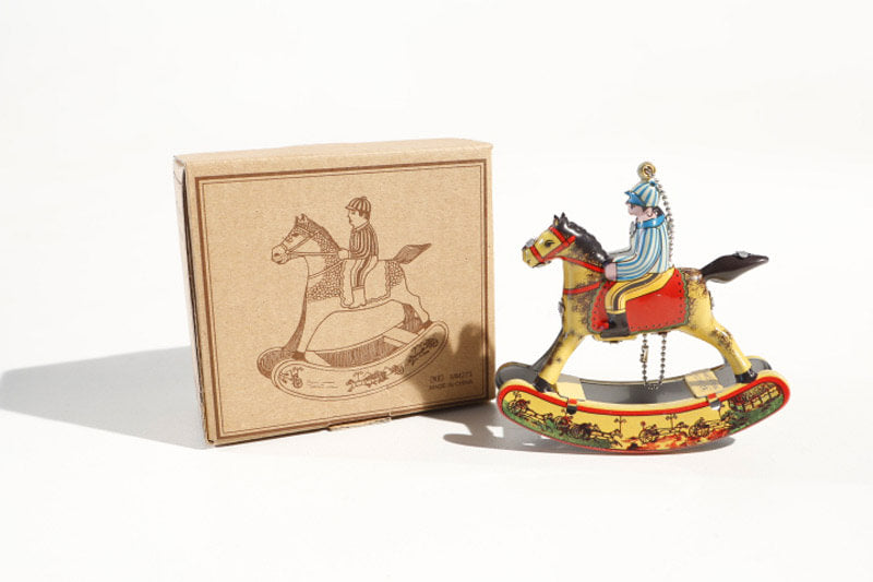 Hanging rocking horse tin toy with rider on, next to its packaging 