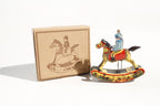 Hanging rocking horse tin toy with rider on, next to its packaging 