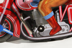 Close-up of a red motorcycle tin toy with a person's leg wearing red boots and blue socks.