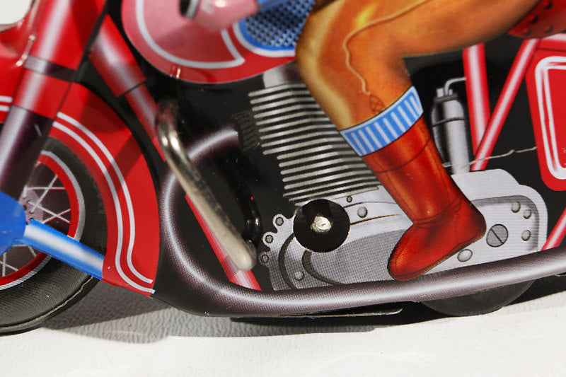 Close-up of a red motorcycle tin toy with a person's leg wearing red boots and blue socks.